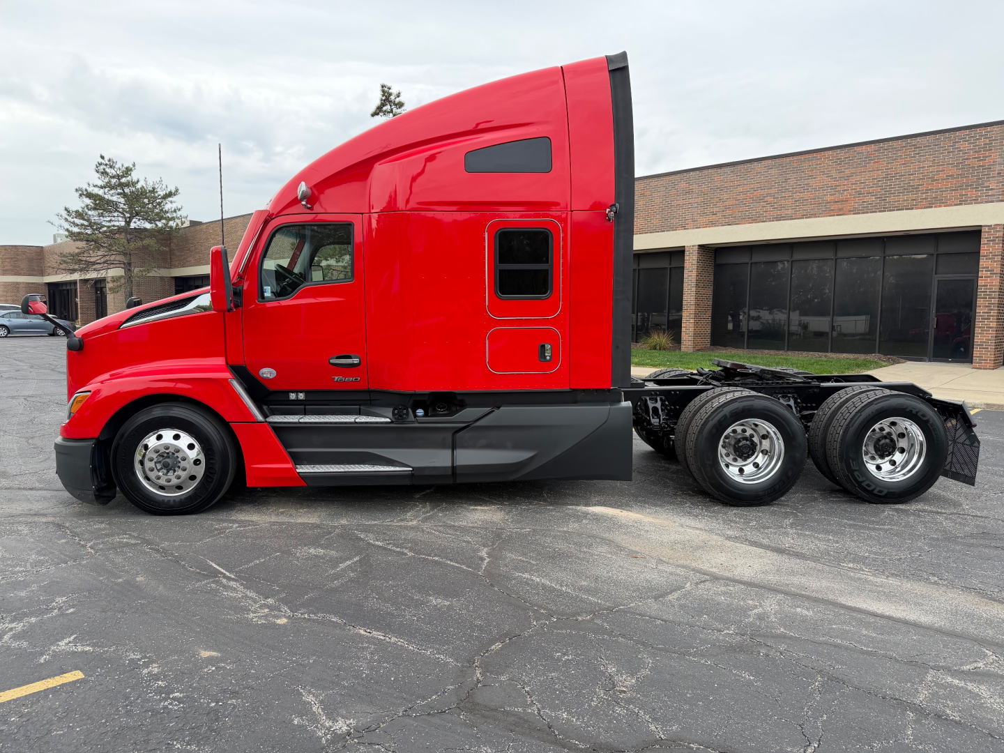 Kenworth T680 tractor cab in red, side view showing sleeper area and rear tandem wheels.