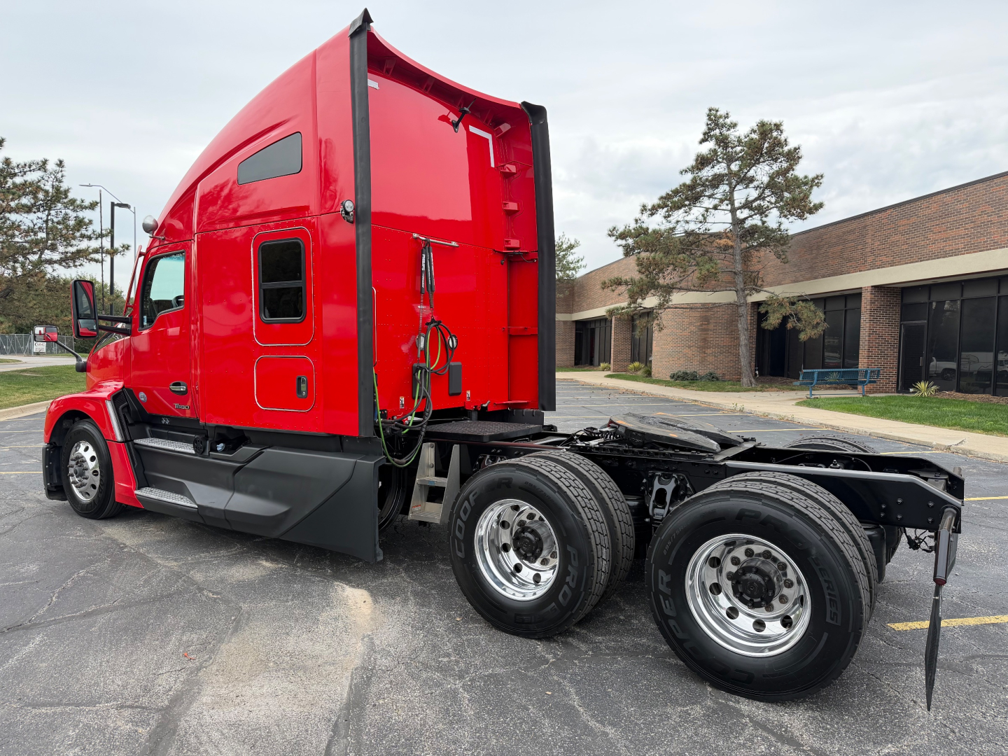 Red Kenworth T680 truck cab with sleeper, side view showing chassis and dual rear axles. Visible text includes VIN label area and Kenworth badge on cab.