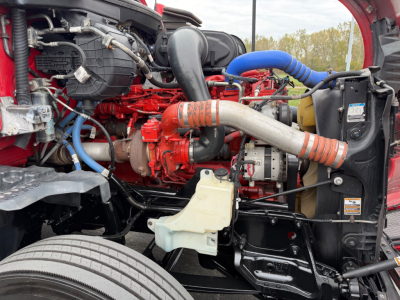 Kenworth T680 engine bay showing large red engine, blue intercooler hoses, white coolant reservoir, and black radiator support.