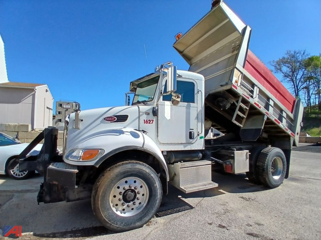 Dump truck in-service Peterbilt 335 with raised dump bed and front fenders, side step, and wheel with hubcap visible.