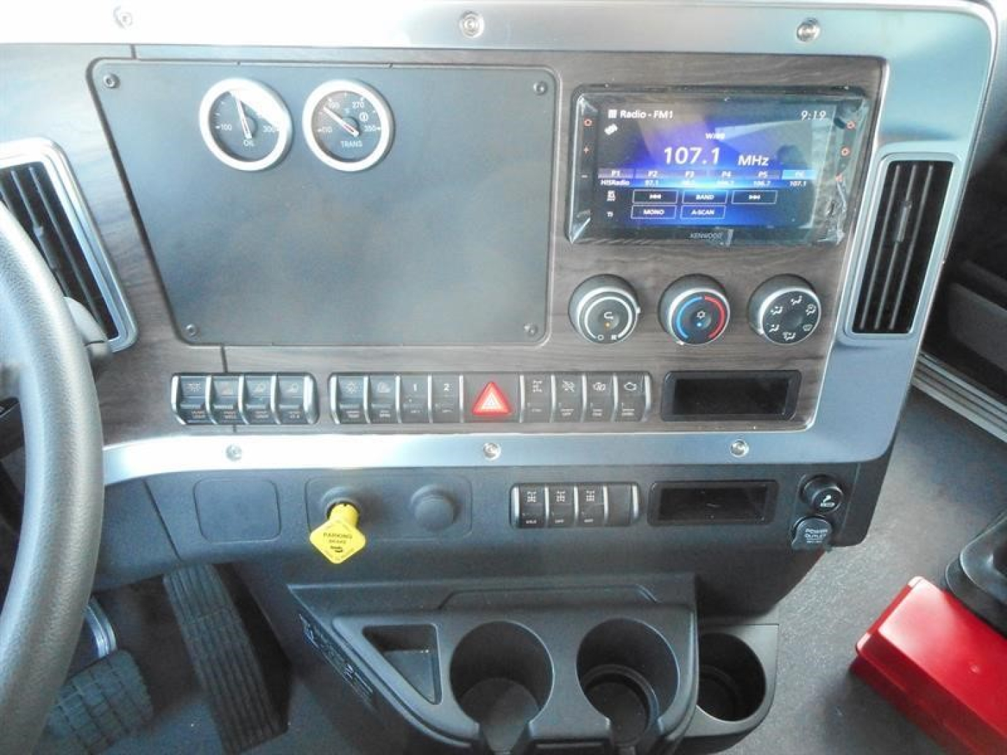 Dashboard of a Western Star 47X dump truck showing gauges, (2) circular meters, touchscreen infotainment, climate controls, hazard button, and cup holders.