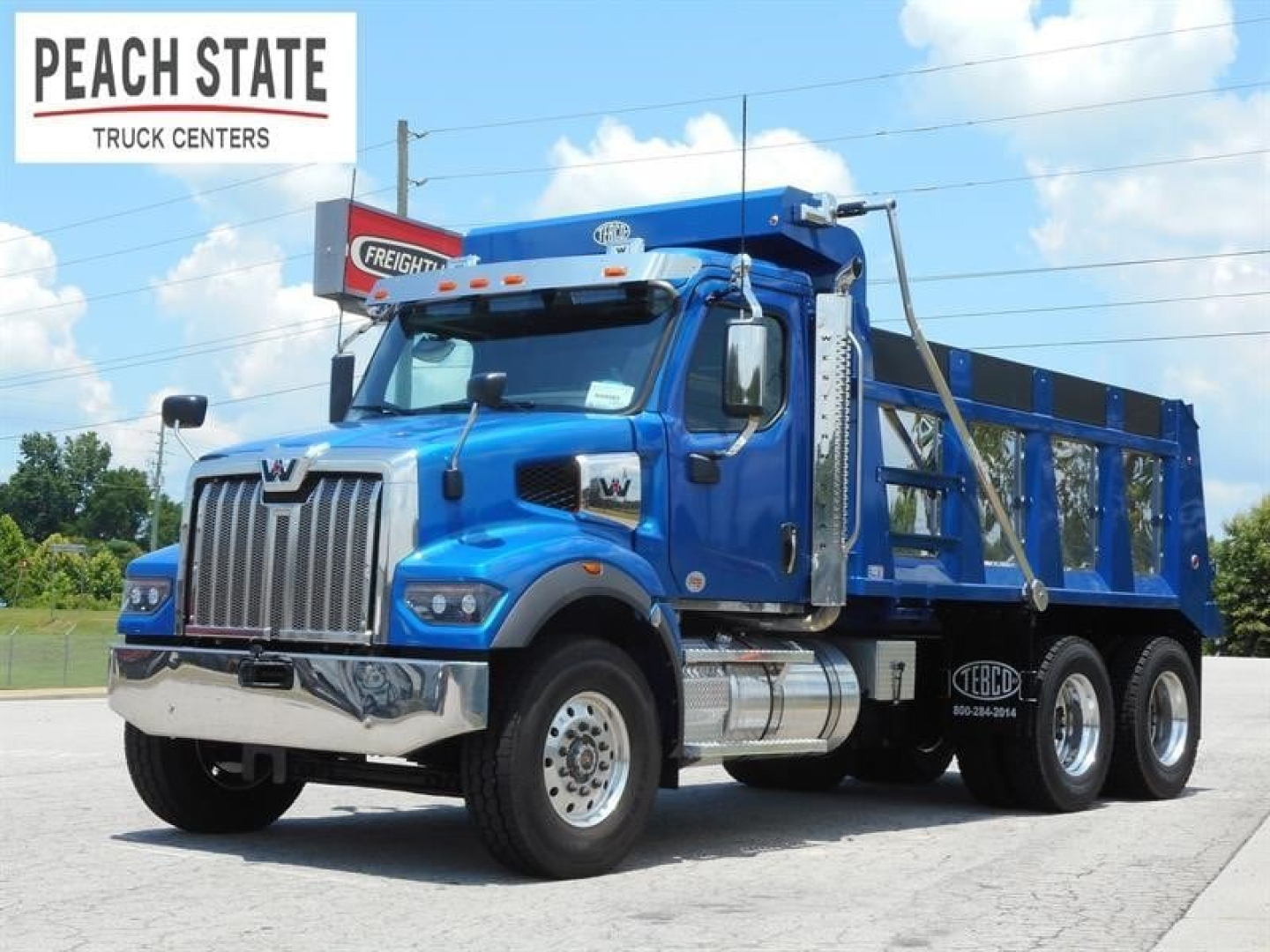 Western Star 47X dump truck in blue, front three-quarter view, showing chrome grille, dual rear axles, and polyethylene dump body. Peach State Truck Centers logo top left.
