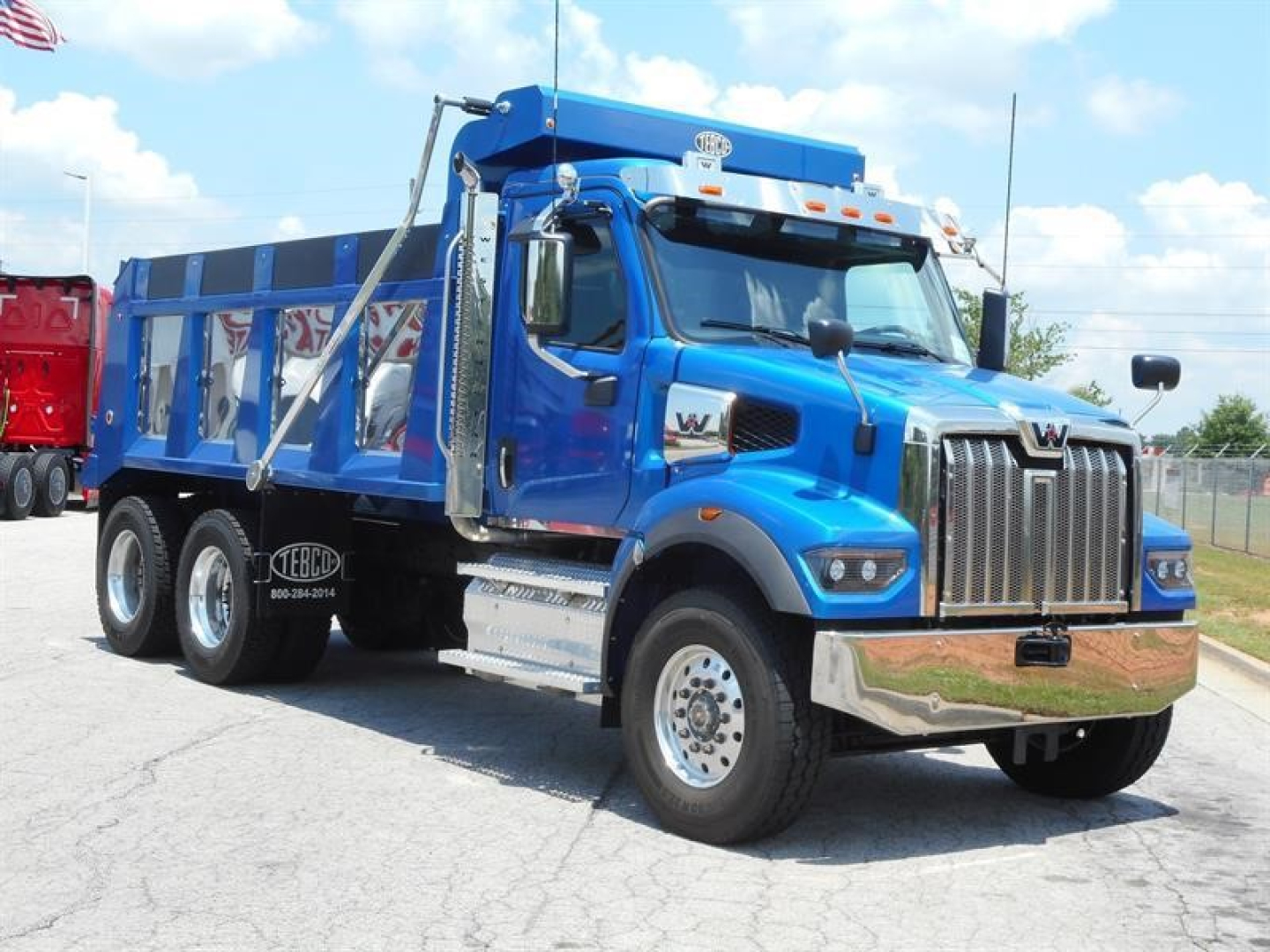 Blue Western Star 47X dump truck with chrome front grille and side guards, three-axle configuration, parked outdoors.