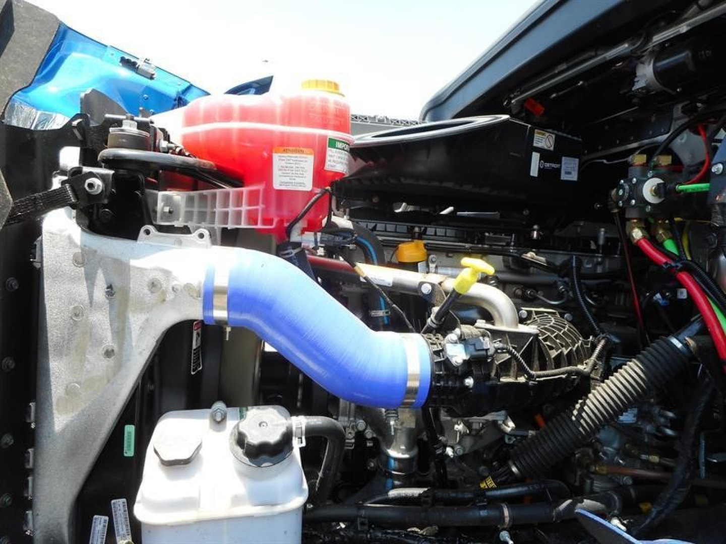 Western Star 47X engine bay showing blue coolant hose, red coolant reservoir, black plastic ducting, and various hoses and metal components.
