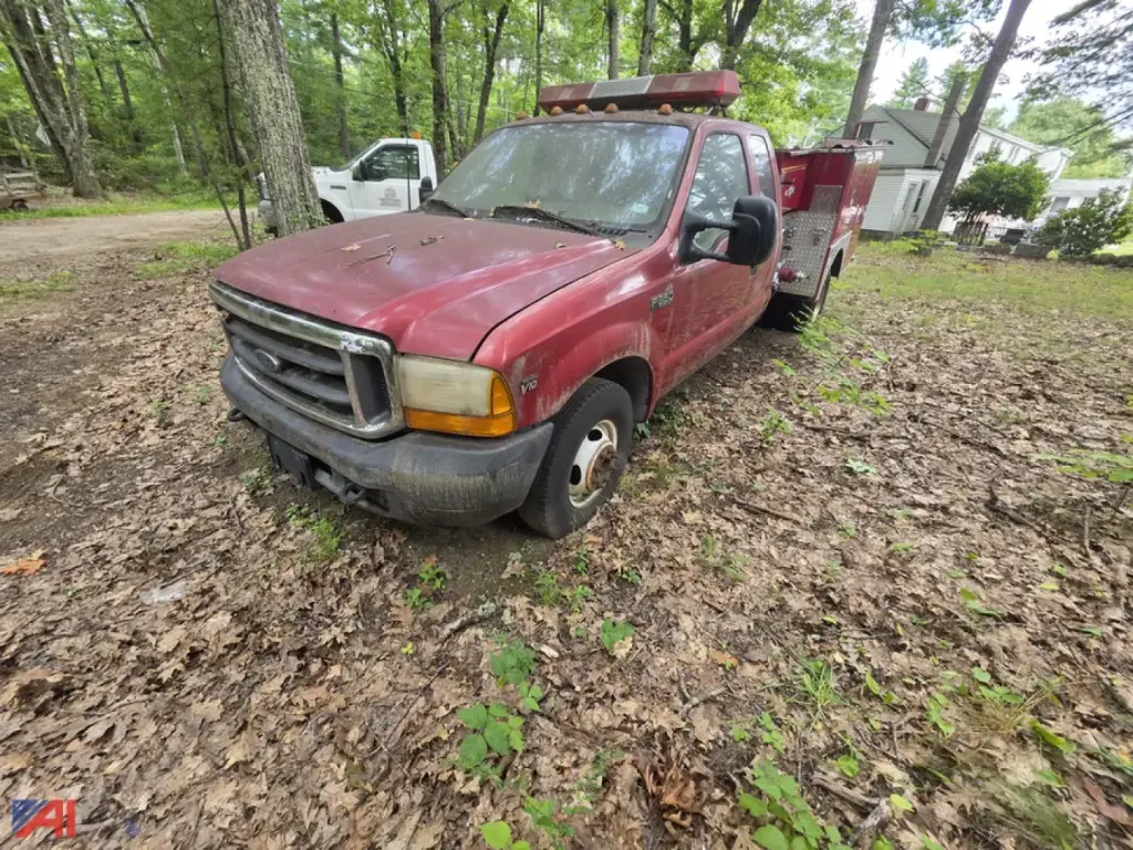 Ford F-350 Super Duty mini pumper fire truck front-left view showing red cab and utility box, light bar on roof, in an outdoor wooded area.