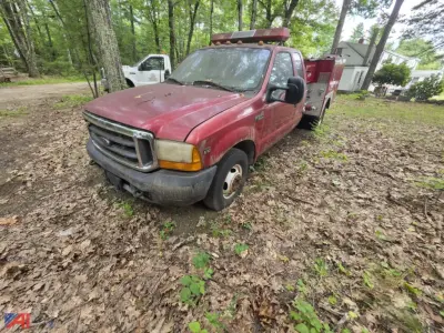 Ford F-350 Super Duty mini pumper fire truck front-left view showing red cab and utility box, light bar on roof, in an outdoor wooded area.