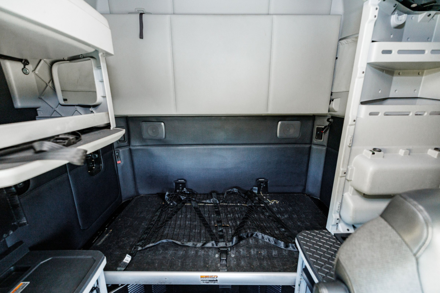 Interior cab view of a 2024 Kenworth T680 sleeper with empty bed area and metal floor, cargo area visible, truck cab components on left and right.