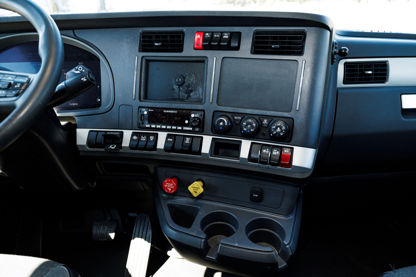 Kenworth T680 dash/center console view showing dashboard with climate controls, radio, cup holders, and storage compartments.
