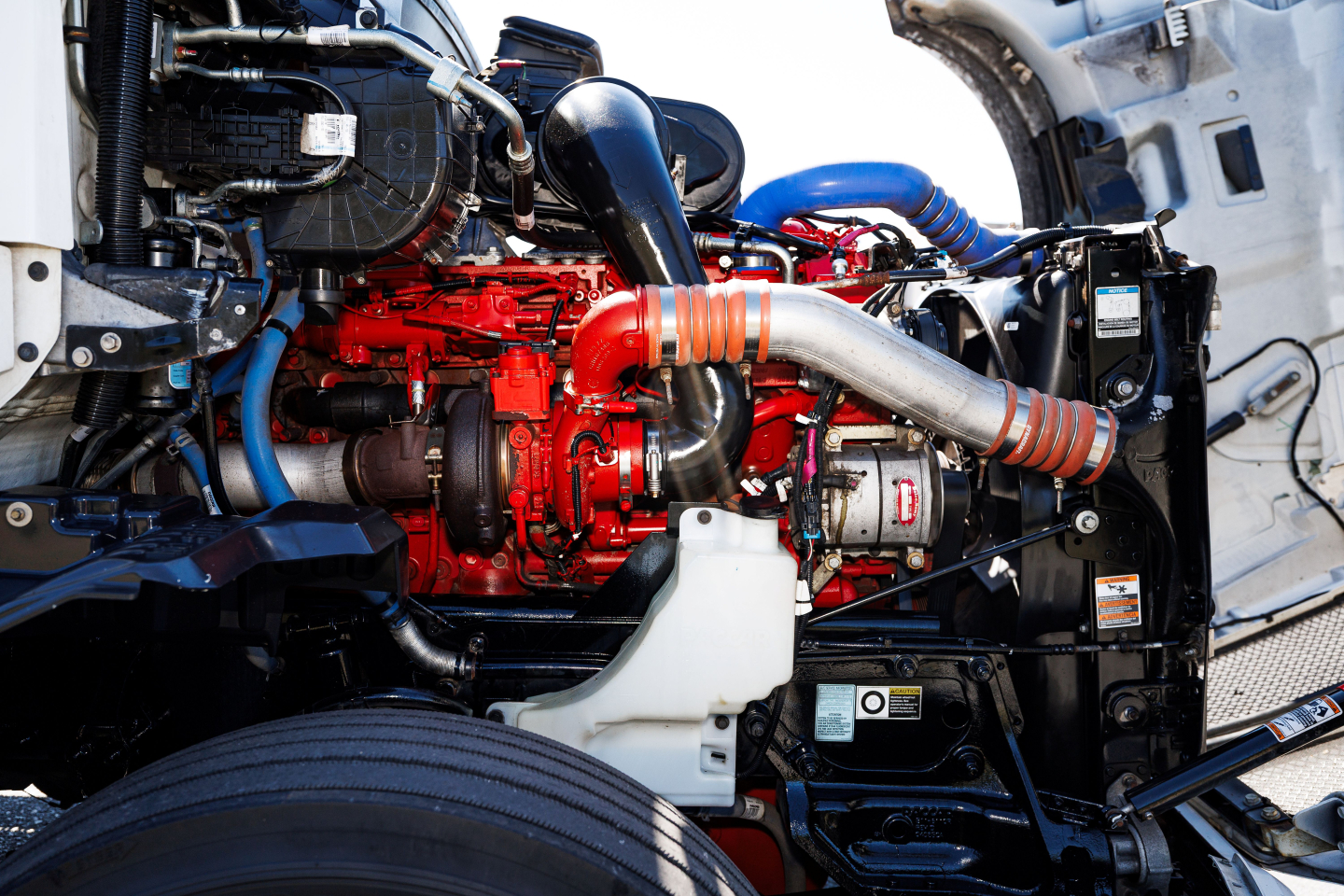 Kenworth T680 engine bay showing red engine block and surrounding blue hoses and components.