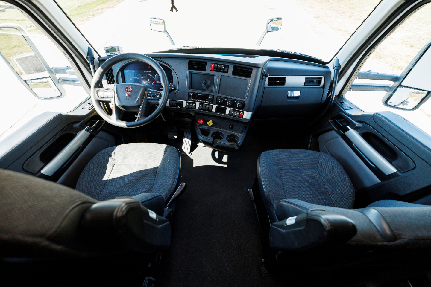 Kenworth T680 truck interior cabin view showing driver and passenger seats, dashboard with steering wheel, control panels, and center console.