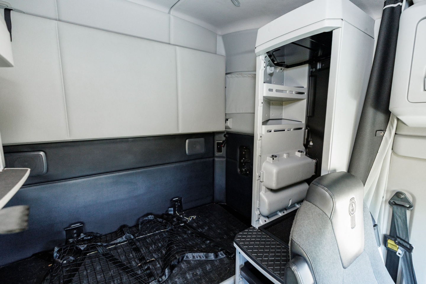Kenworth T680 sleeper cab interior showing front passenger seat, open bunk/cab area, and storage compartments with white interior panels.
