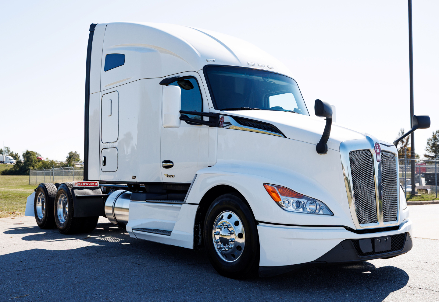 Kenworth T680 sleeper cab truck in white, side view showing front grille, headlights, and dual rear axles.