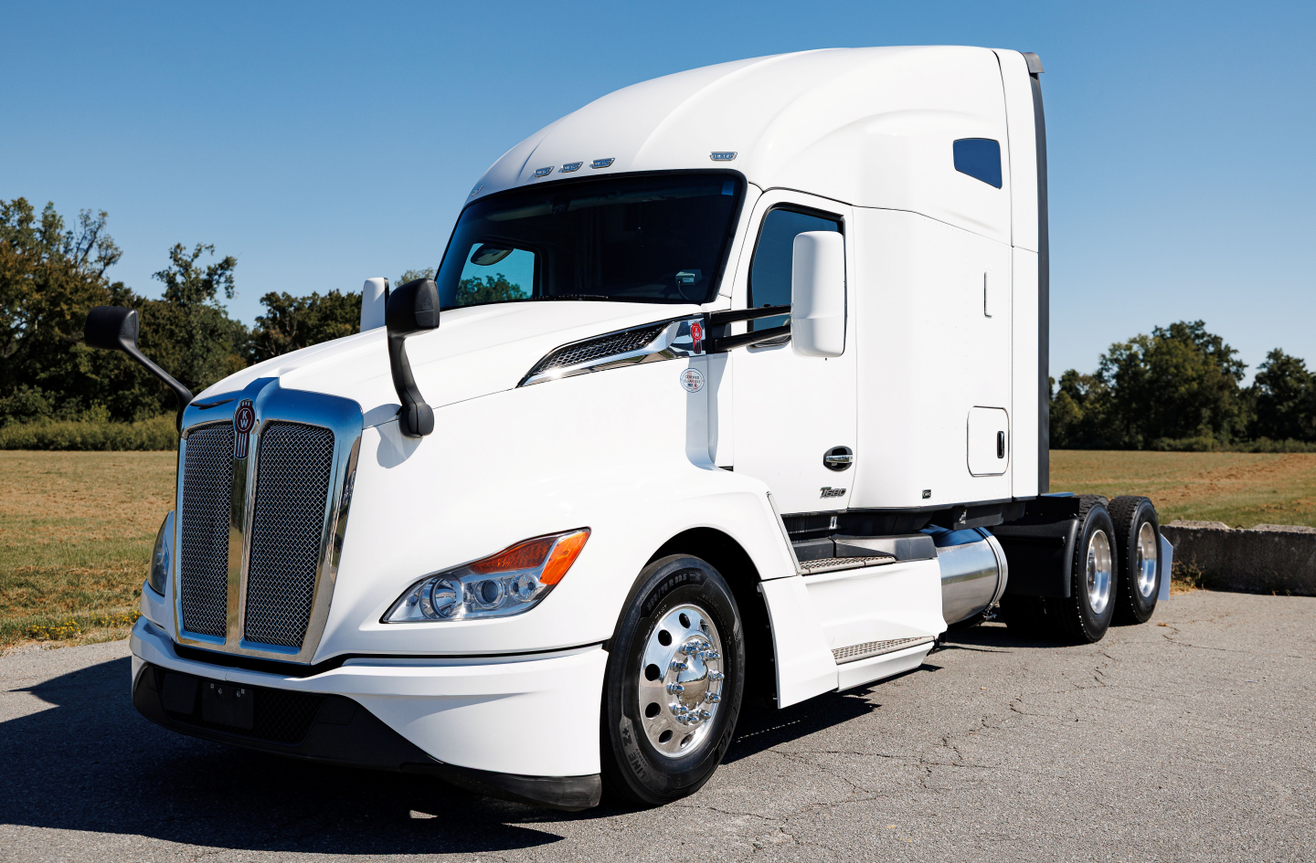 Kenworth T680 conventional sleeper tractor in white, front left angle, chrome grille, dual rear axles, badge details on hood