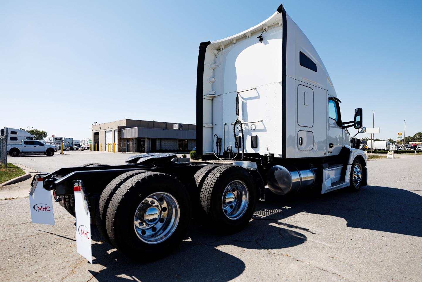 Kenworth T680 semi-truck rear/side view showing chrome wheels, fifth wheel, and sleeper cab with white exterior.