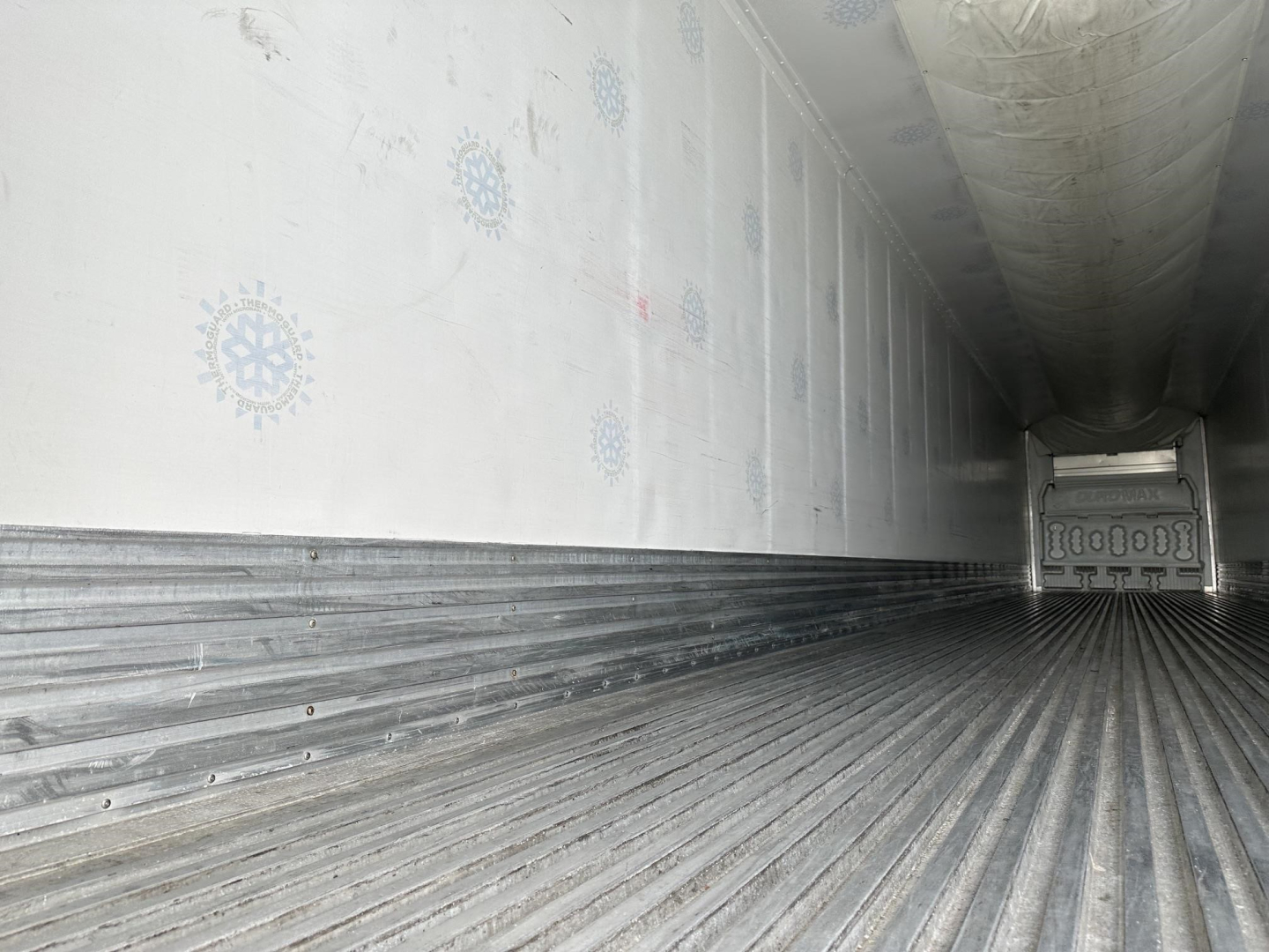 Interior of a used reefer trailer showing ribbed metal floor and side walls with circular refrigeration logos and a rear door.