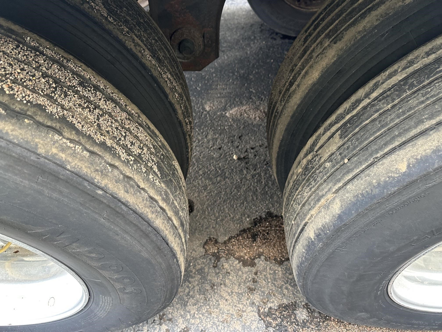 Dual rear trailer tires with dirt and grime on the treads and a glimpse of the chassis between them.