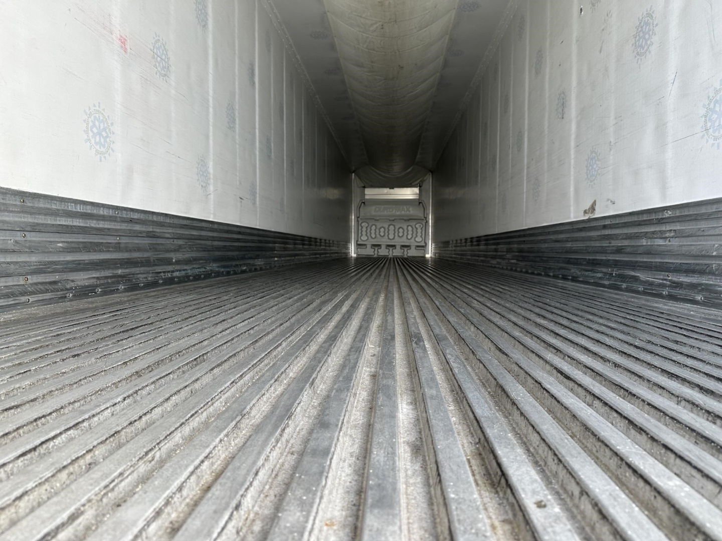 Trailer interior showing ribbed metal floor and insulated walls, rear door with latch visible at far end.