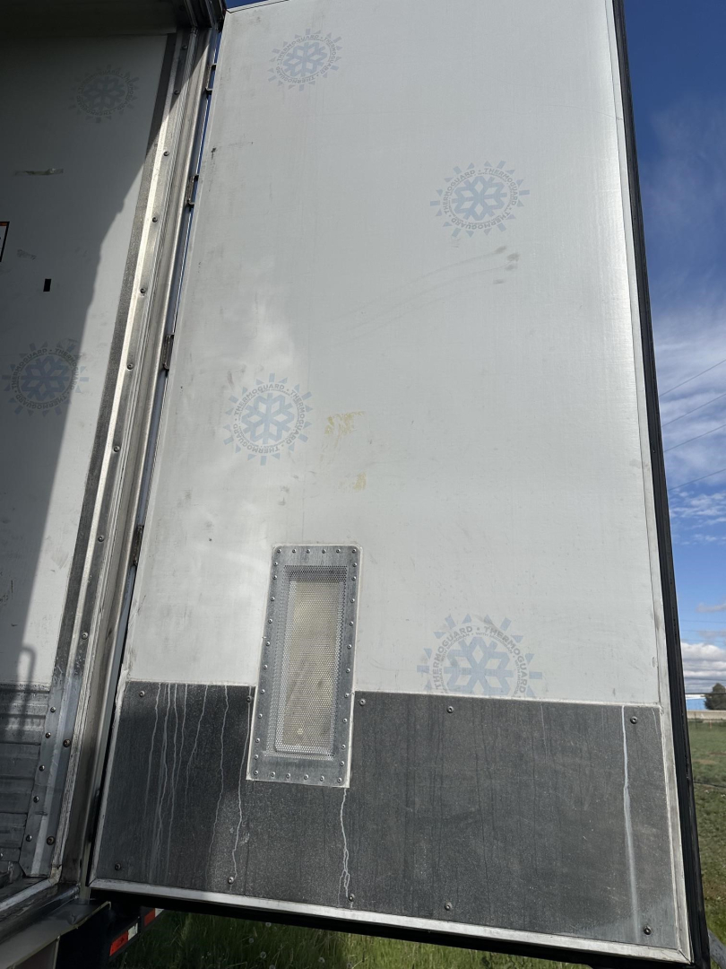 Reefer trailer side showing white and gray exterior with a small vertical rectangular access door and faint blue snowflake graphics.