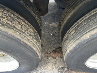 Dual rear trailer tires with dirt and grime on the treads and a glimpse of the chassis between them.