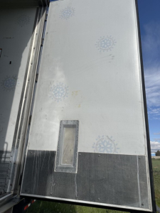 Reefer trailer rear door with vertical window panel and snowflake logo pattern; plain light gray surface with darker lower panel, no legible serials visible.