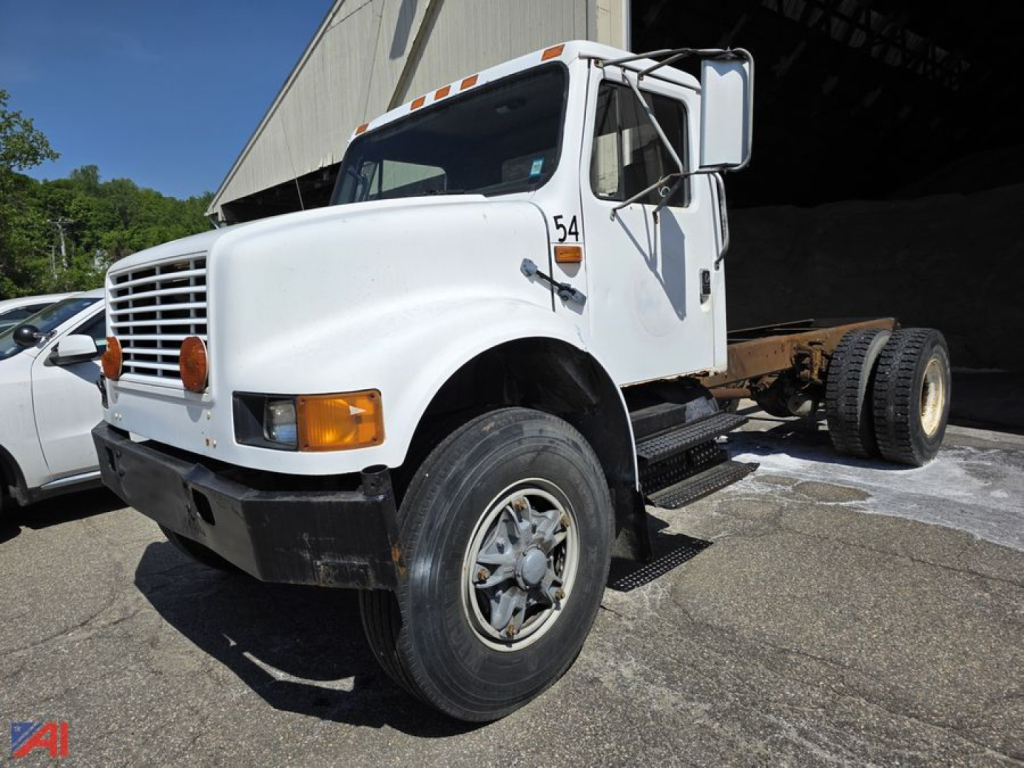 International 4700 cab and chassis with white cab, front grille, orange marker lights, single rear axle, exposed chassis, side steps, and large front tire.
