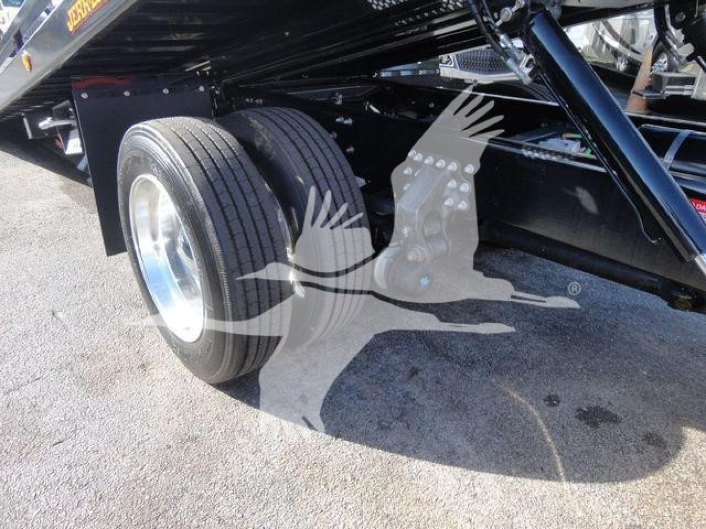 Dual rear wheels of a truck chassis showing suspension and black frame with reflection on cement.