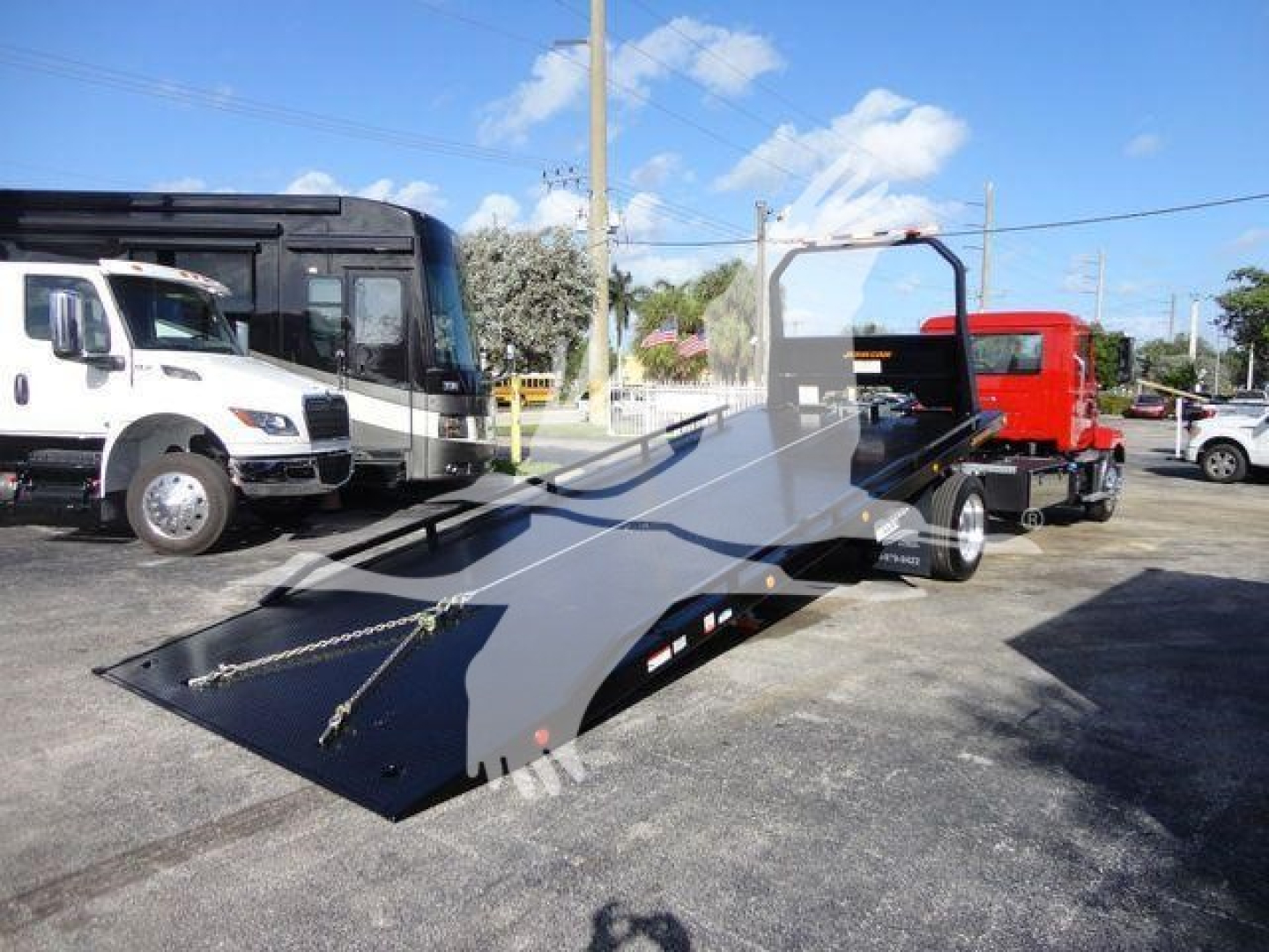 Mack MD6 rollout truck flatbed in dealership lot with white and black trucks in background.