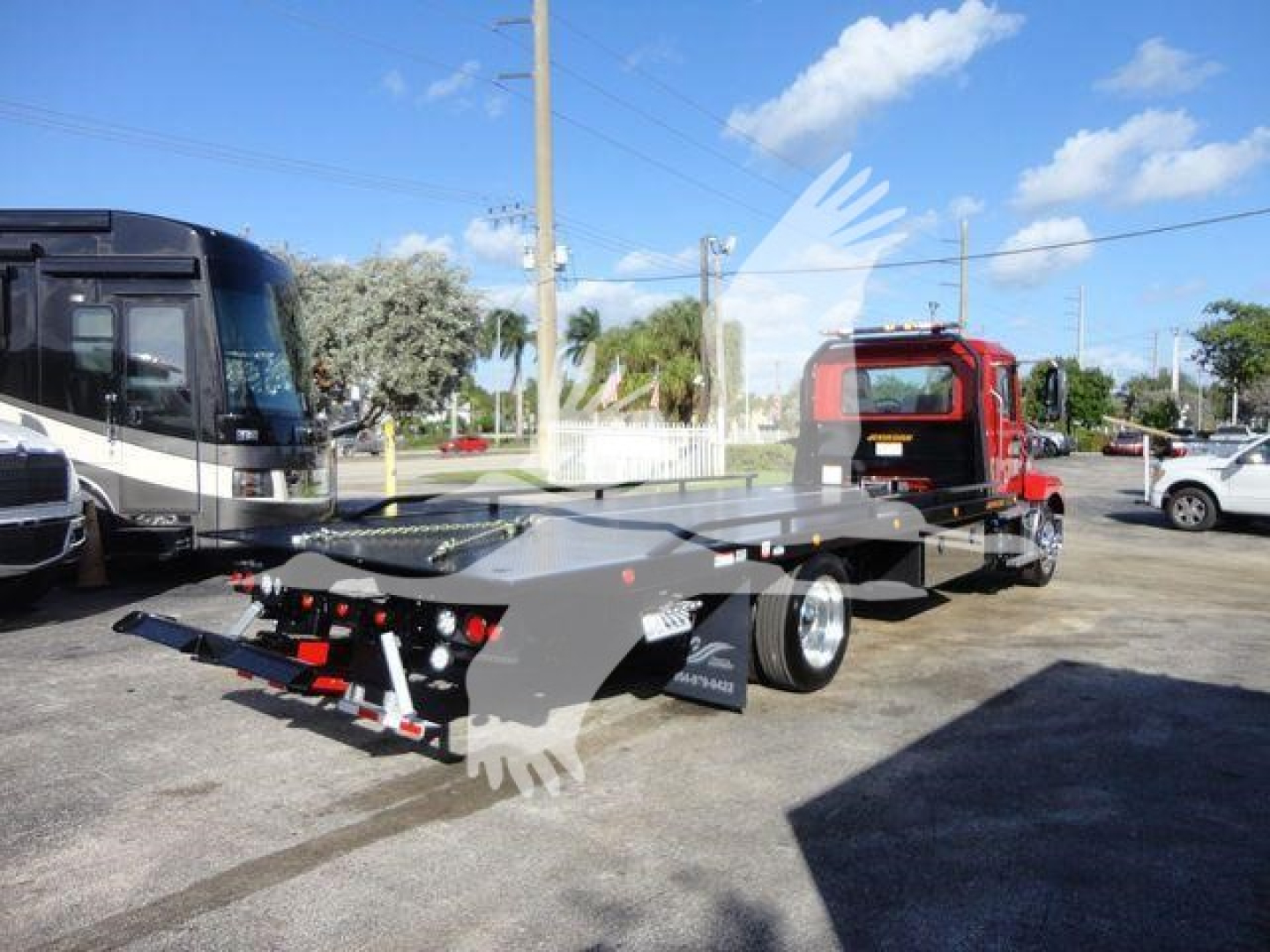 MD6 rollback truck in a parking lot showing a lowboy trailer with a red cab and black chassis, rear lights, and safety equipment, stock number J07243.
