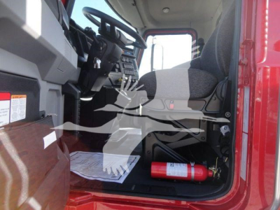 Mack MD6 truck cab interior view showing driver seat and dashboard with steering wheel, papers on floor, and a red fire extinguisher mounted under dash.