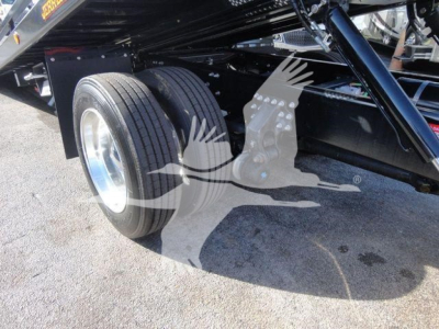 Dual rear wheels of a truck chassis showing suspension and black frame with reflection on cement.