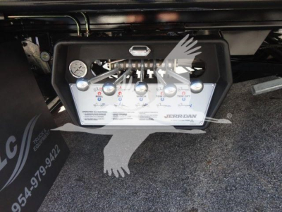 Panel with gauges and control valves labeled with GPM/PSI and letters; a hydraulic manifold with several levers and a small gauge, mounted under a truck, with a Jaz Jordan label.