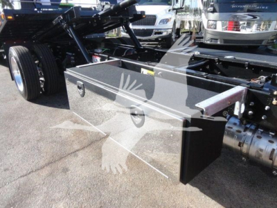 Truck chassis with a large side toolbox mounted on the frame, showing the toolbox lid and mounting area; background includes other trucks.