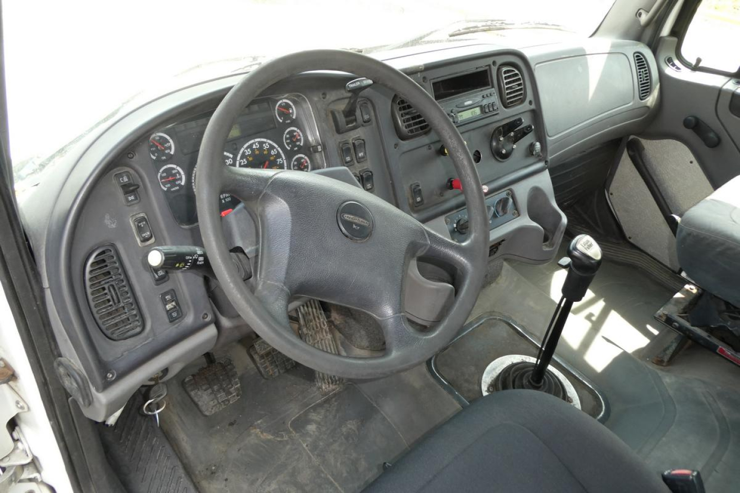 Cab interior of 2007 Freightliner M2 112 with manual shifter, steering wheel, instrument cluster, and dashboard controls visible.