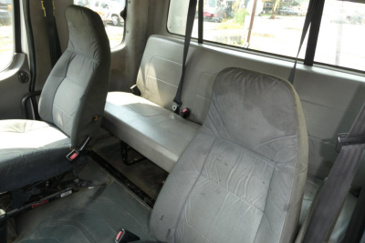 Interior of a used 2007 Freightliner M2 112 cab showing aftermarket cloth seats and a bench in back with seatbelts.