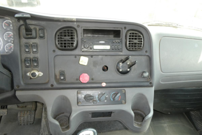 Dashboard panel of a Freightliner M2 112 daycab showing radio, vents, knobs, and switch cluster.