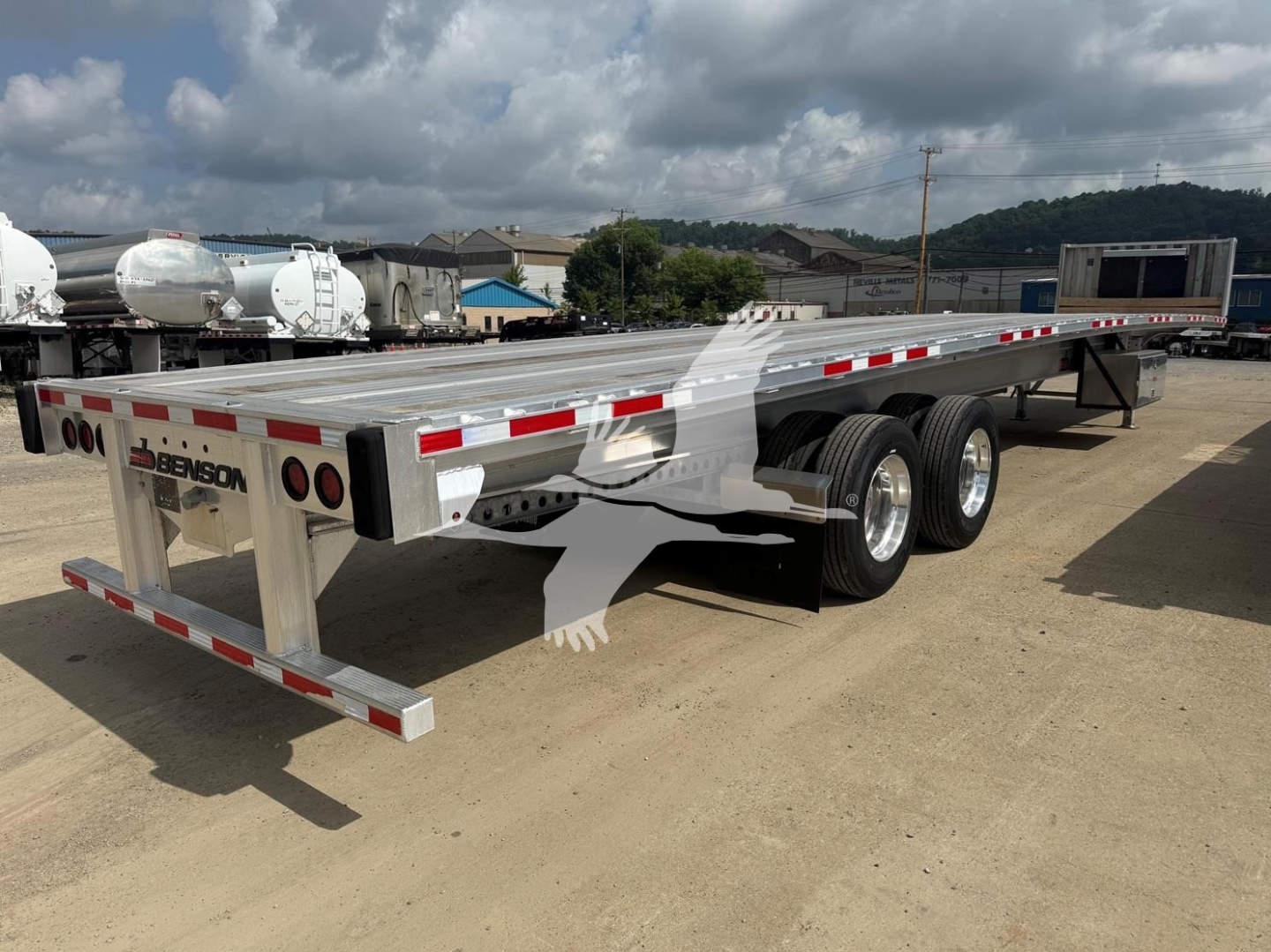 Flatbed trailer showing Benson branding, dual rear axles, metal deck with reflective stripes, side rails, and rear bumper lights.