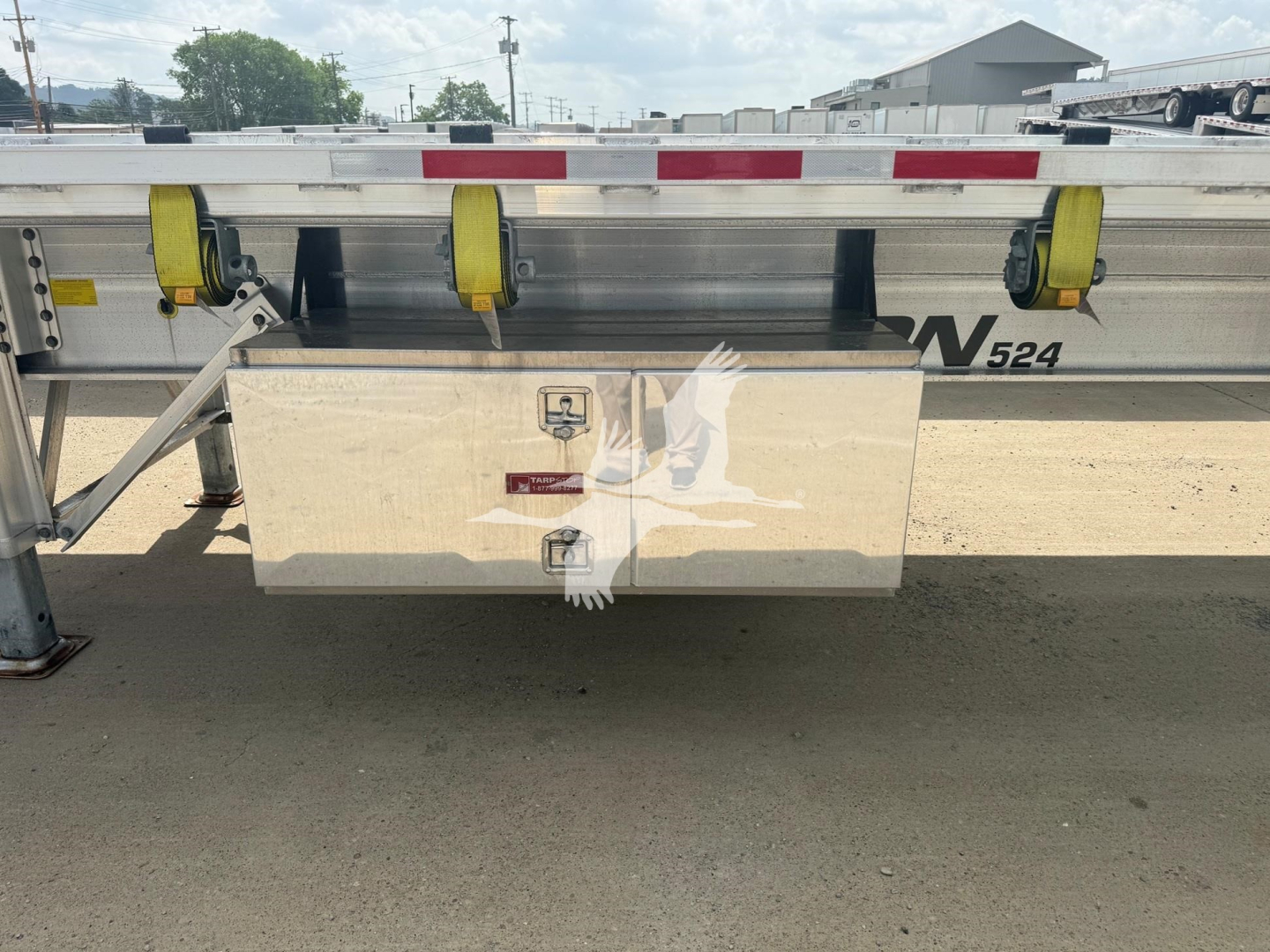 Flatbed trailer side showing storage box and tie-down straps with Benson branding and reflective tape.