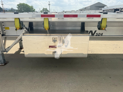 Flatbed trailer side showing storage box and tie-down straps with Benson branding and reflective tape.