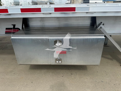 Flatbed trailer toolbox mounted under trailer with aluminum diamond plate lid and two latching handles.