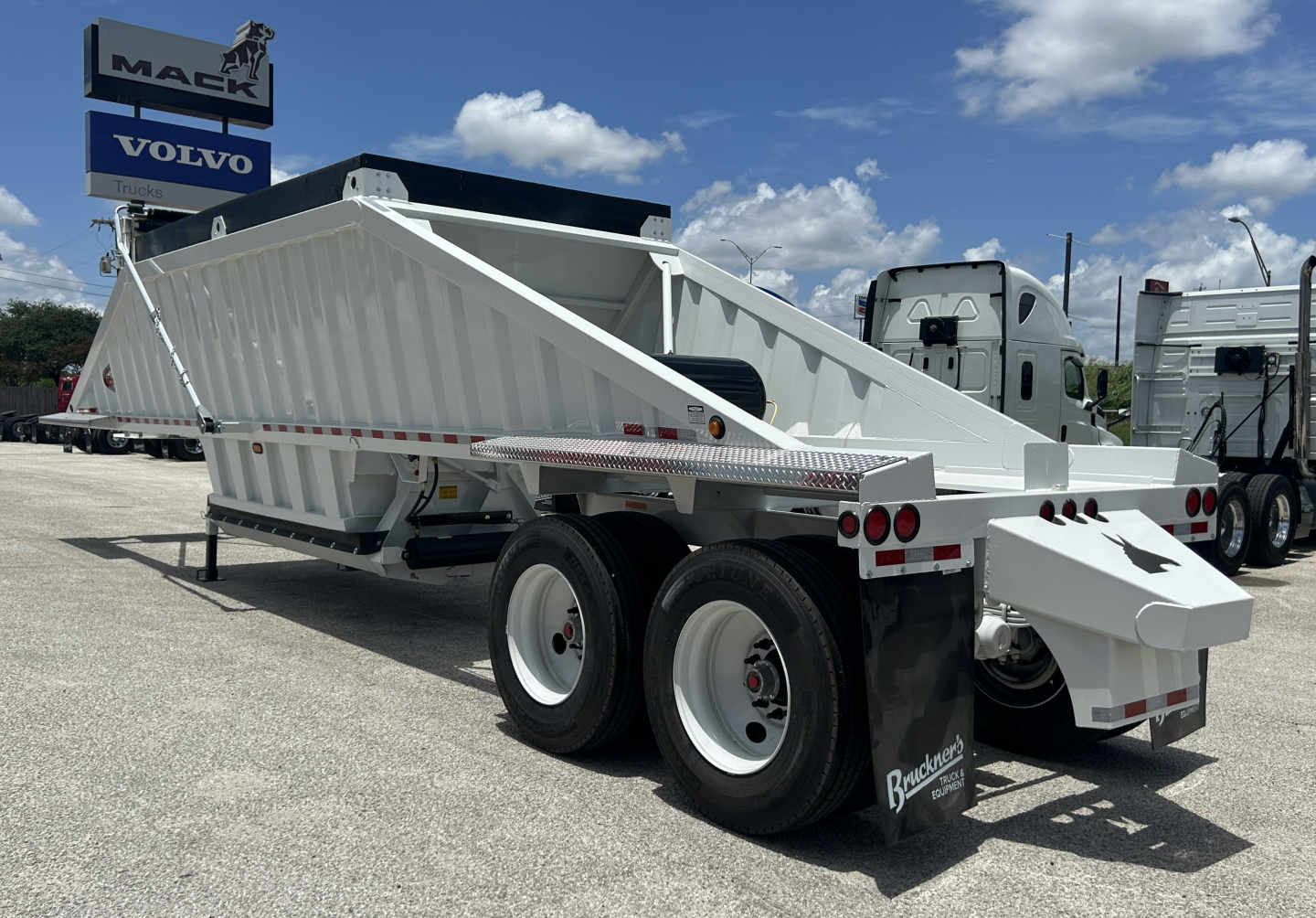 Trailer dump bed dual rear axles white tilt trailer viewed from side rear showing open-top dump body and tandem wheels.