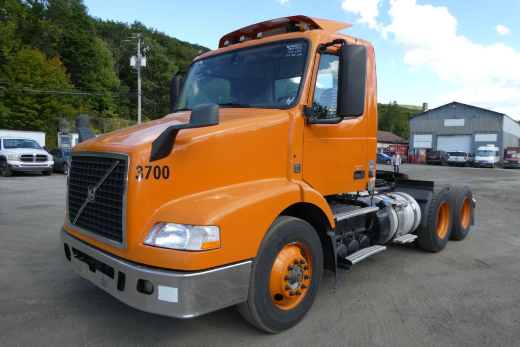 Orange Volvo VNM64T conventional daycab truck showing front and side view with 3700 printed on door and dual rear axles.