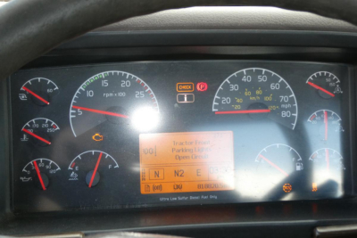 Dashboard of a Volvo truck showing multiple gauges and a central digital display. Visible text includes ‘Tractor Front Parking Lights Open/Off’, warning icons, and various RPM/temperature scales.
