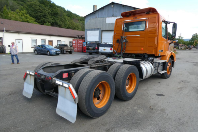 Volvo VNM64T conventional daycab tractor rear view showing chassis, dual rear axles, orange cab, and fuel tanks.