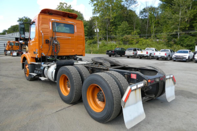 Volvo truck cab and chassis in orange, rear view showing dual rear axles with large tires and mud flaps.