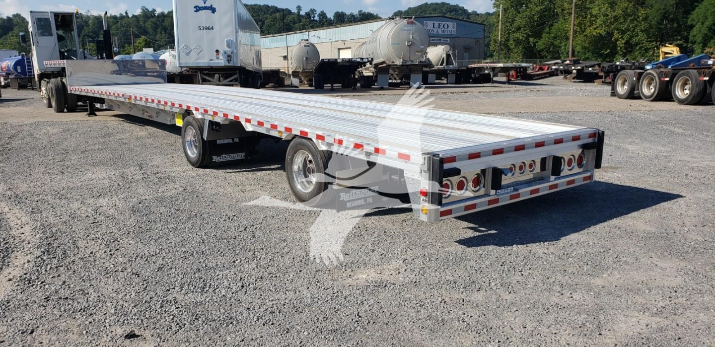 Big Bubba trailer flatbed showing rear with multiple taillights and reflective tape along sides under clear sky.