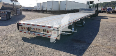 Flatbed trailer with long aluminum deck and rear lights, parked in a lot; rear bumper with circular brake lights and white reflective trim.