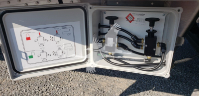 Trailer compartment with open panel showing hose connections and schematic diagram inside door. Visible hoses, fittings, and a warning label.
