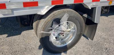 Trailer wheel and fender area of a 2027 Reitnouer Big Bubba trailer showing dual wheels, mudflap, and reflective tape on the side.