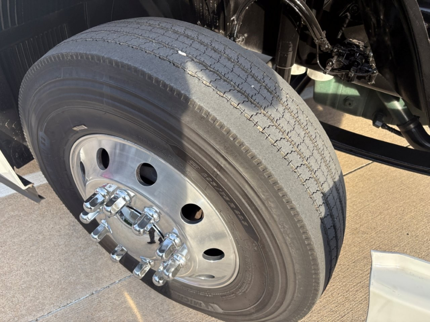 Wheel and tire showing front dual axle with metallic lug nuts and hub cover; tread visible but worn; part of Volvo VNR truck front axle in a daycab.