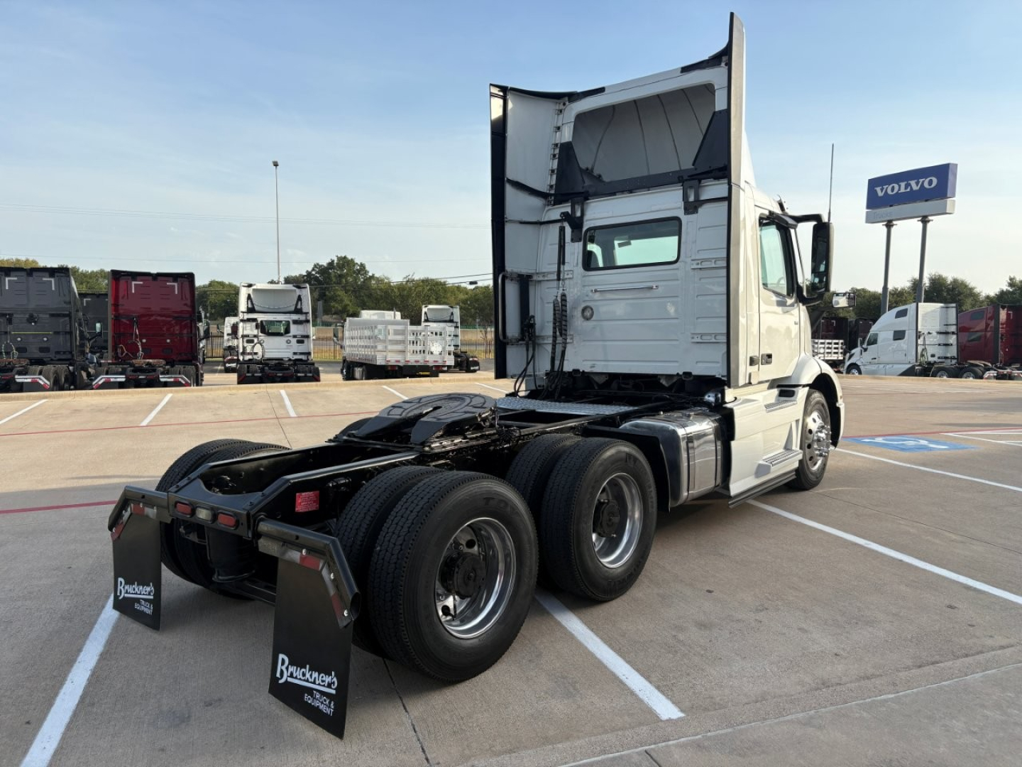 Volvo VNR64T300 daycab truck rear view showing tandem dual rear axles and white sleeper cab, with Volvo dealership in background